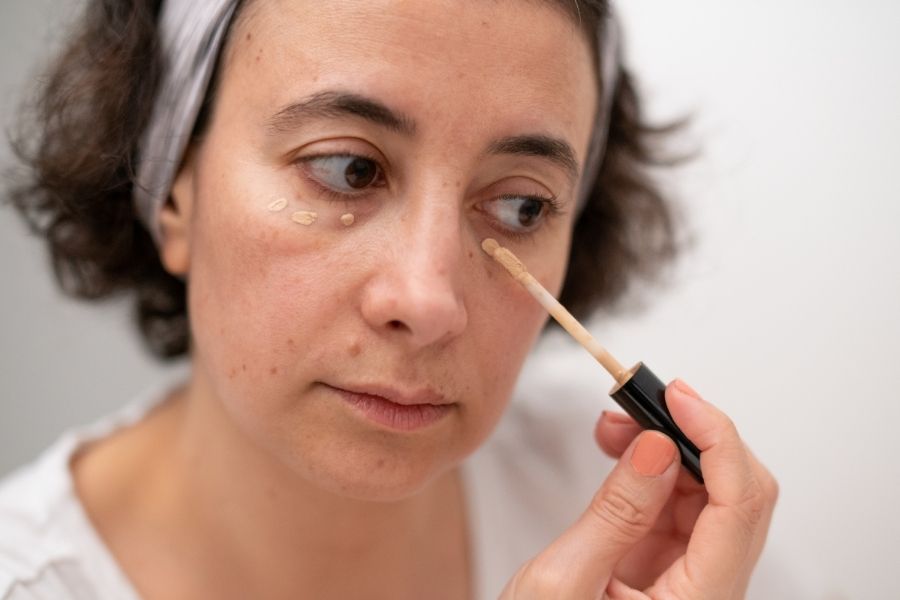 Woman applying concealer mapping technique with makeup brush near eye area