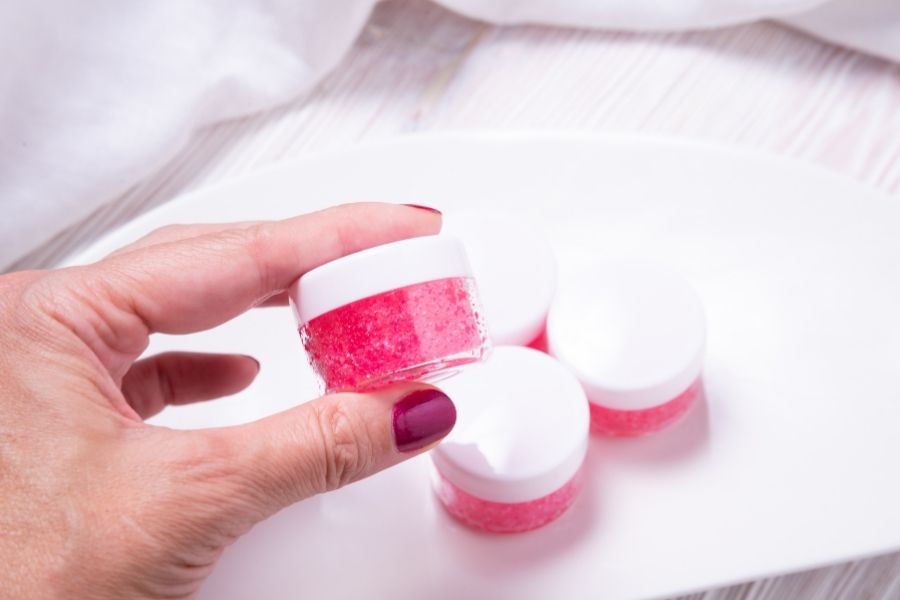 Hand holding homemade DIY lip scrubs in small glass jars with pink granulated texture