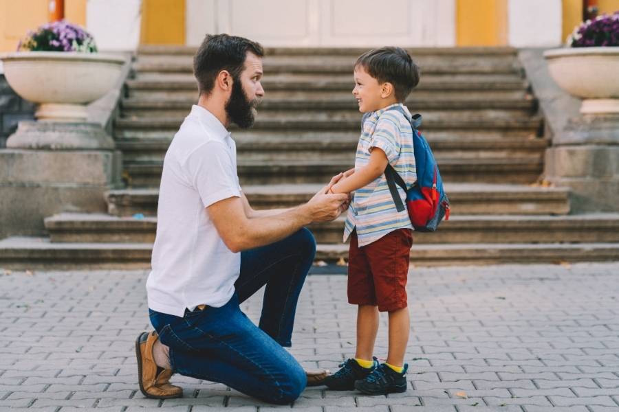 Father kneeling down to child's eye level demonstrating gentle parenting approach before school in urban setting