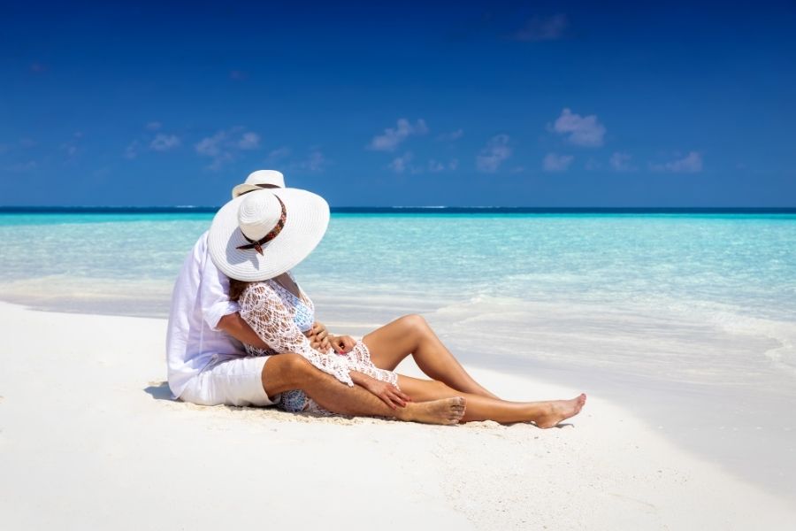 Woman in white sun hat relaxing on tropical beach focusing on honeymoon skincare protection