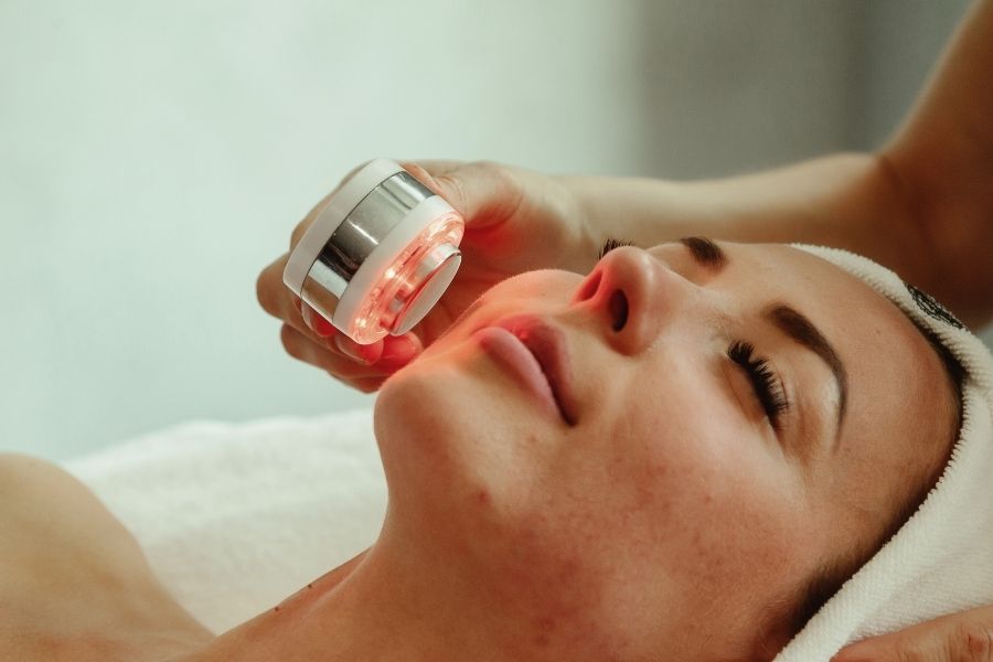 Woman receiving LED light therapy treatment with red light device at spa