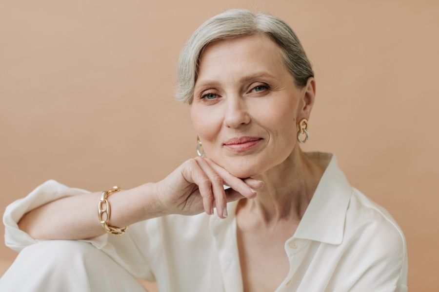 Elegant woman with silver hair showcasing minimalist beauty in neutral tones and gold jewelry