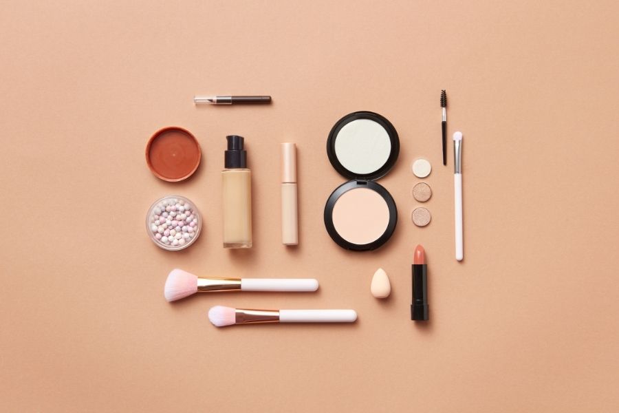 Flat lay of monochromatic makeup products in neutral tones on beige background