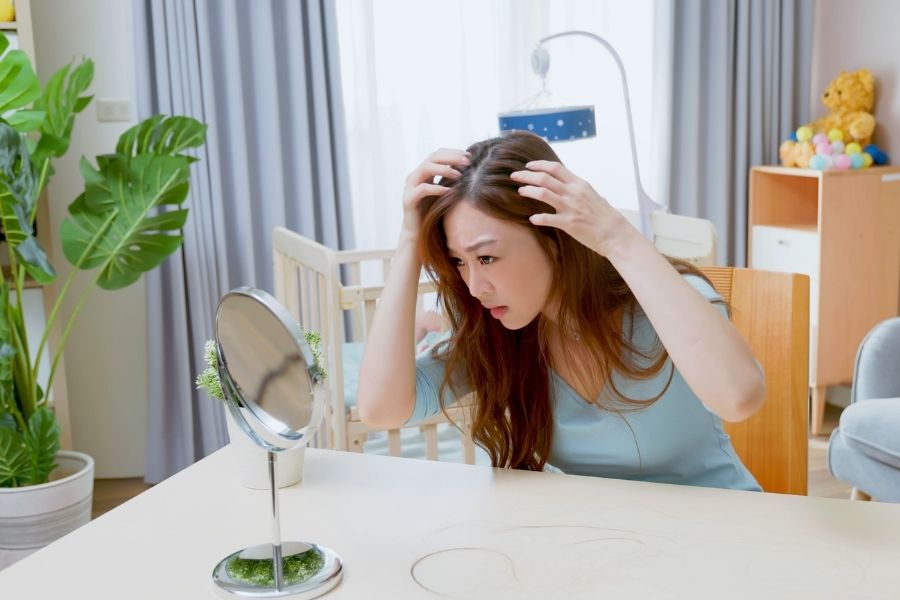 Woman examining her hair in mirror showing signs of postpartum hair loss in home setting