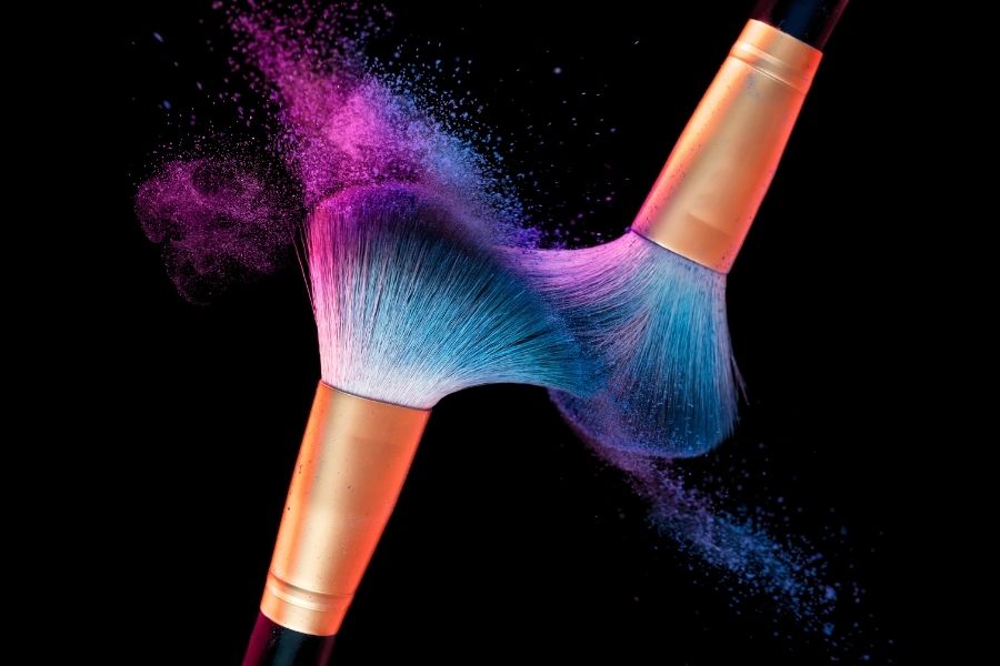 Professional makeup brush with vibrant pink and blue powder explosion for quick makeup application