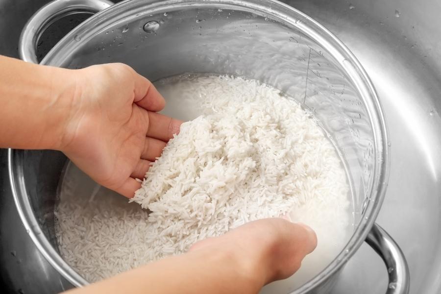 Hands washing rice in clear bowl for preparing homemade rice water rinses hair treatment