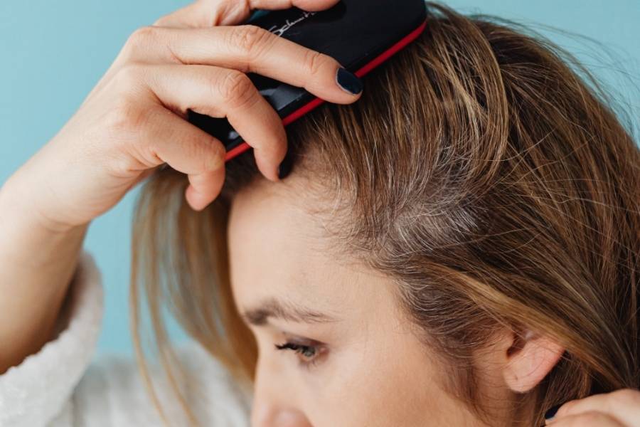 Woman using scalp detox massage tool with red bristles for deep cleansing treatment