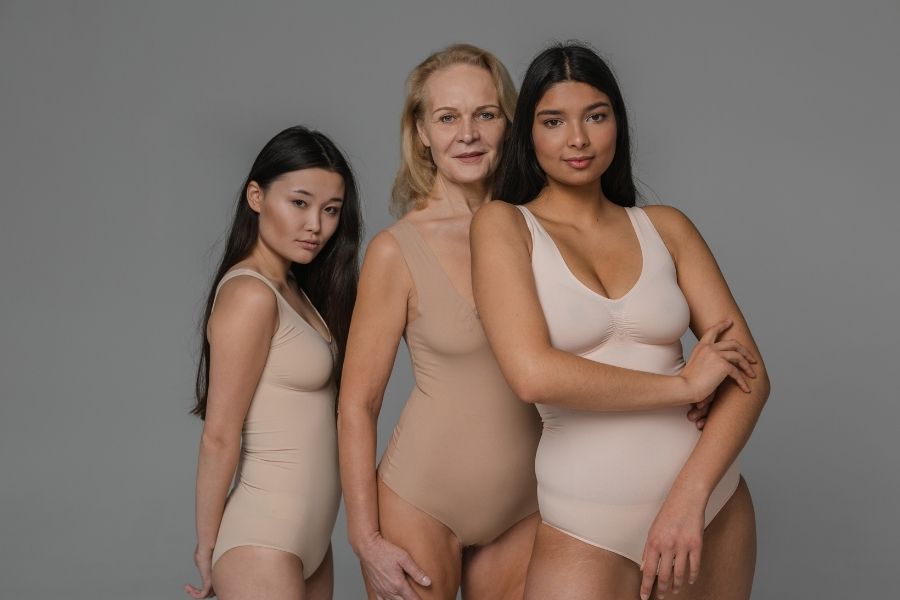 Three diverse women modeling nude-toned shapewear in different body types and ages