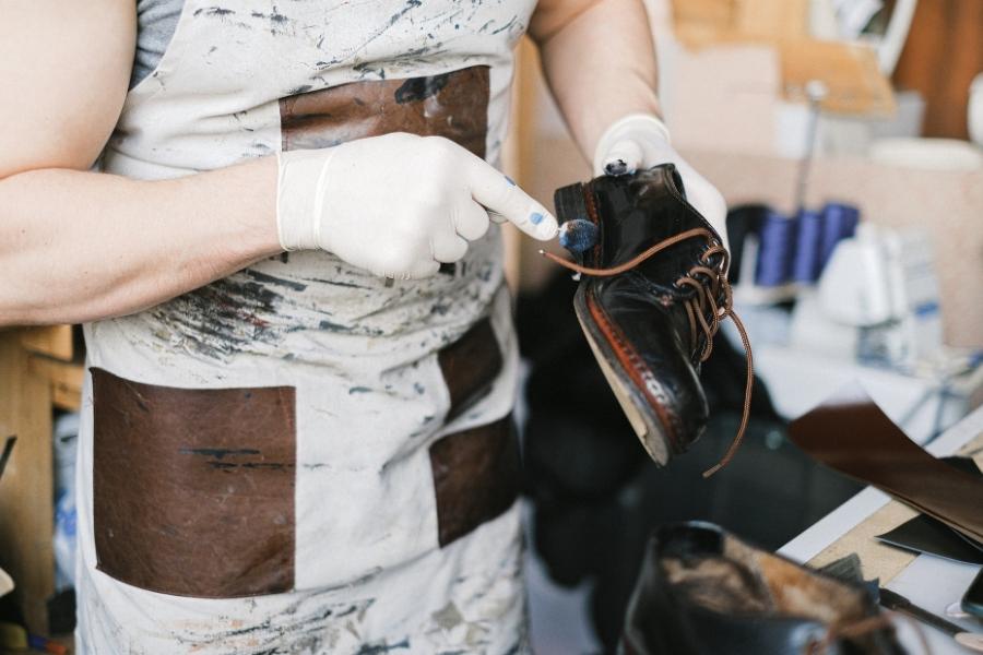 Artisan performing professional shoe care on leather boot with specialized tools in workshop