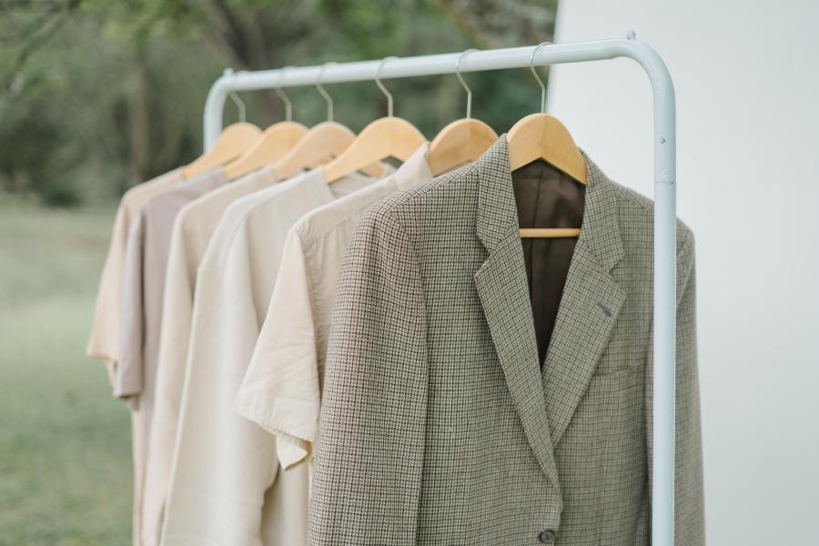 Sustainable fashion clothing rack with neutral blazer and shirts on wooden hangers outdoors