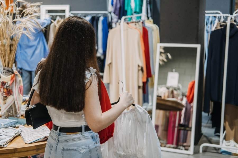 Woman shopping for transitional pieces in clothing store with colorful garments and mirror