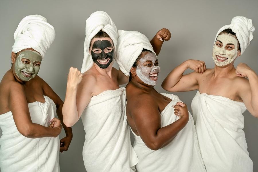 Four diverse women in towels enjoying wedding day skincare treatments with face masks