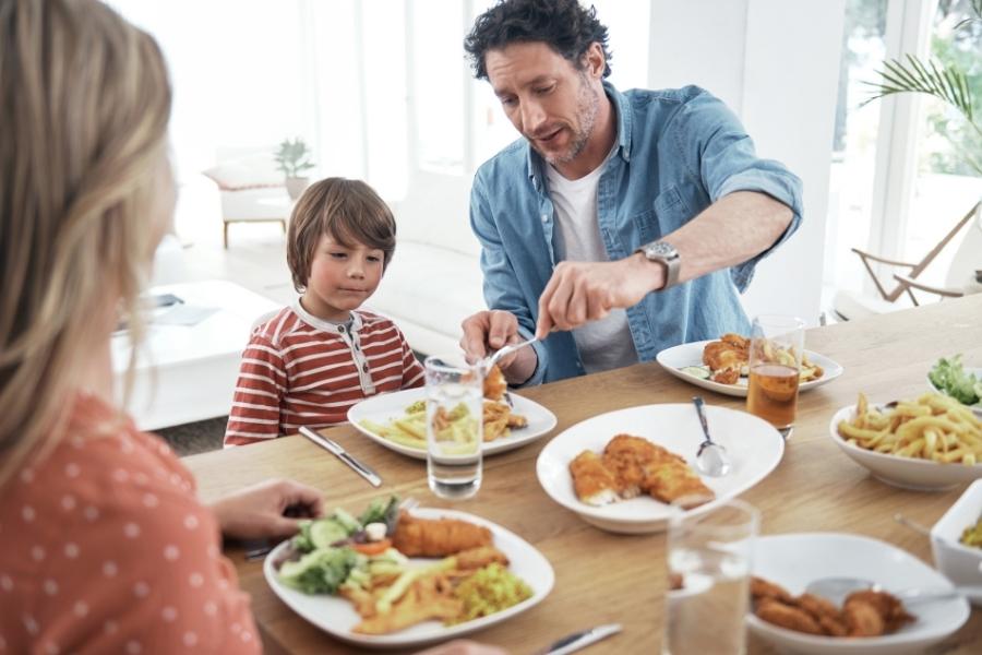 Father serving food to his young son during a warm family dinner gathering in bright modern dining room