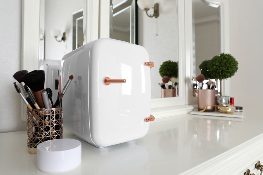 Modern organized vanity setup featuring white beauty refrigerator and rose gold accessories