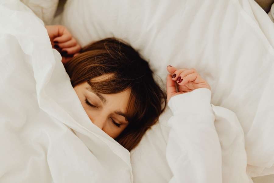 A woman sleeping uneasily under white covers, representing the impact of poor sleep quality.