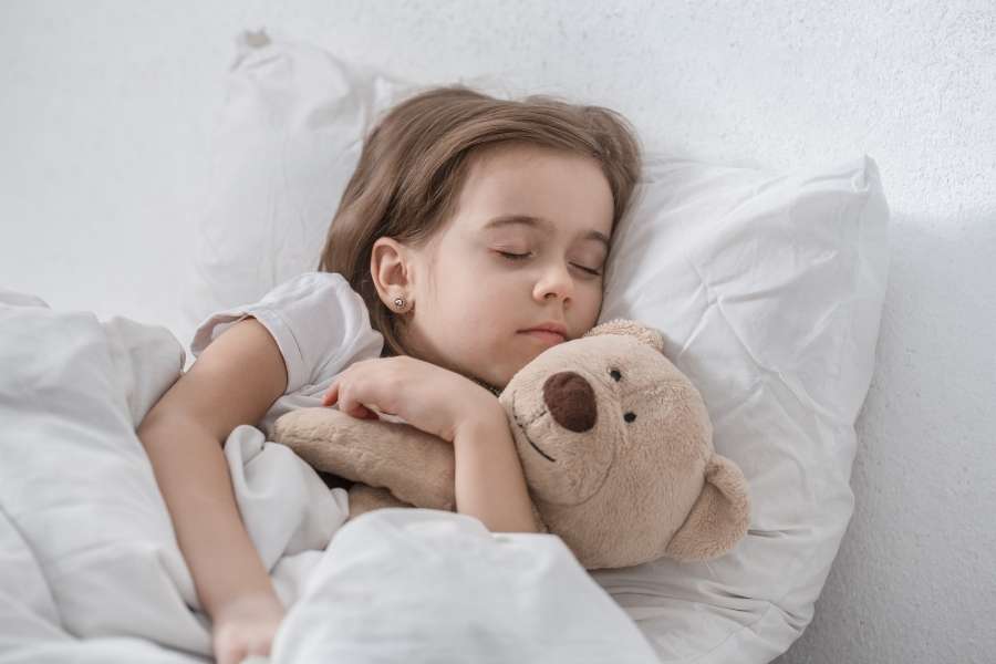 A peaceful young girl sleeping deeply in bed while hugging her teddy bear, related to a toddler suddenly refusing to sleep.